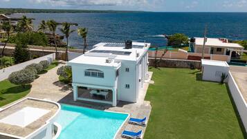 A modern house with a swimming pool, sun loungers, and a view of the ocean.