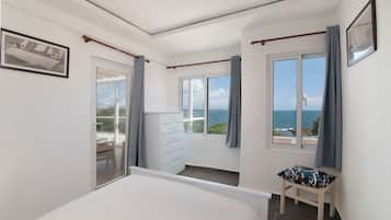 A bedroom with a bed, a dresser, a chair, and a view of the sea.