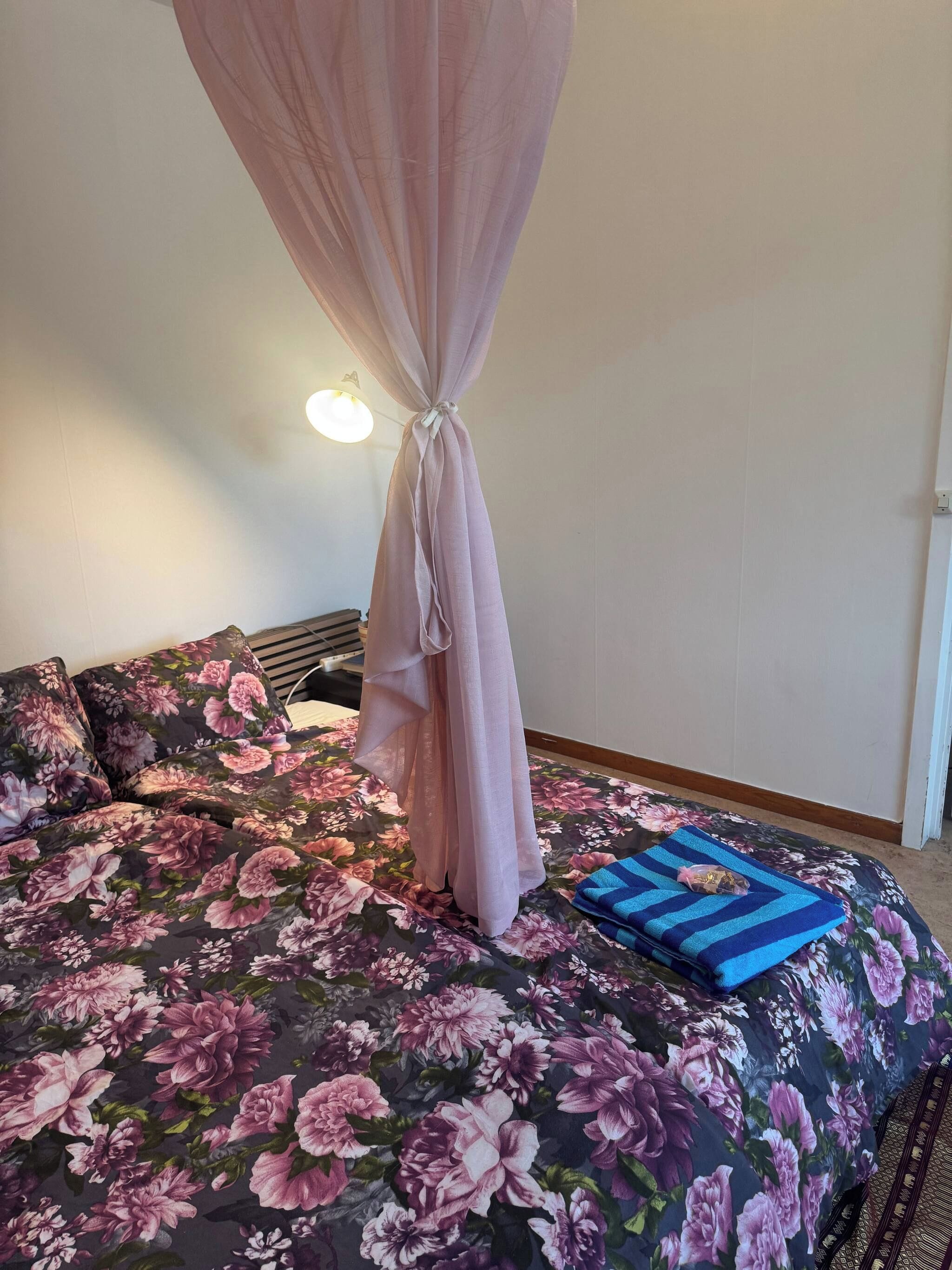 Una cama con colcha estampada, una toalla azul a rayas y un dosel rosa.