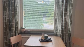 A room with a table, two chairs, a hanging light fixture, a window with blinds, and a radiator.