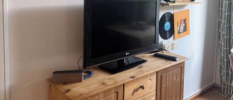 A room with a television on a wooden cabinet, wall-mounted records, and framed pictures.