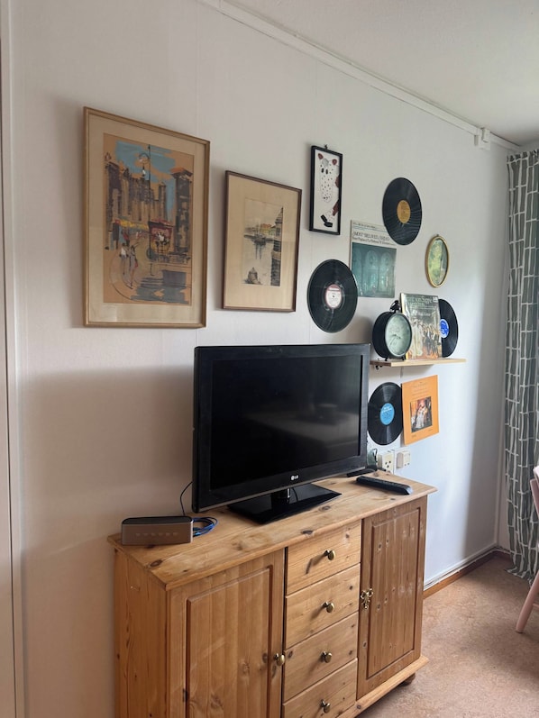 Una habitación con un televisor sobre un mueble de madera, discos colgados en la pared y fotografías enmarcadas.