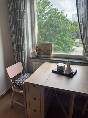 Una habitación con escritorio, silla, ventana con vista y un cuadro enmarcado.