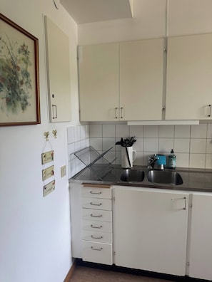 Una cocina con armarios blancos, un lavamanos y una encimera con una tetera y dispensador de jabón.