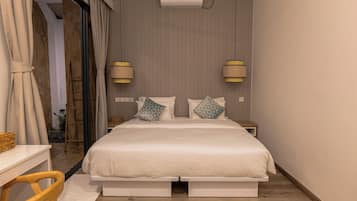 A bedroom with a bed, two bedside lamps, a wall-mounted air conditioner, and a wooden floor.