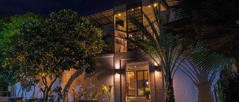 A modern building with a glass facade, outdoor seating, and a palm tree.