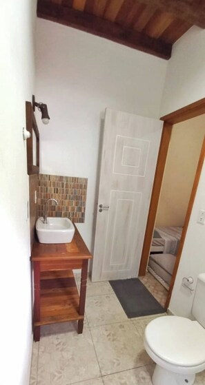 A bathroom with a white sink, wooden vanity, tiled backsplash, and a white toilet. - Vacation home on Rua da Praia da Feiticeira. (Ilhabela)
