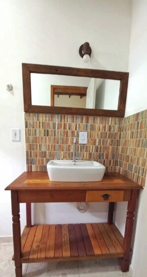 A bathroom with a wooden vanity, a white sink, and a mirror above it. - Vacation home on Rua da Praia da Feiticeira. (Ilhabela)