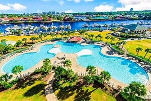 A large, irregularly shaped swimming pool surrounded by palm trees and lounge chairs, with a marina and buildings in the background. - Barefoot Resort N. Myrtle Beach: Golf & Beach (North Myrtle Beach)