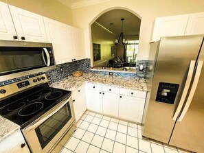 A kitchen with white cabinets, a stainless steel refrigerator, a microwave, and a stove. - Barefoot Resort N. Myrtle Beach: Golf & Beach (North Myrtle Beach)