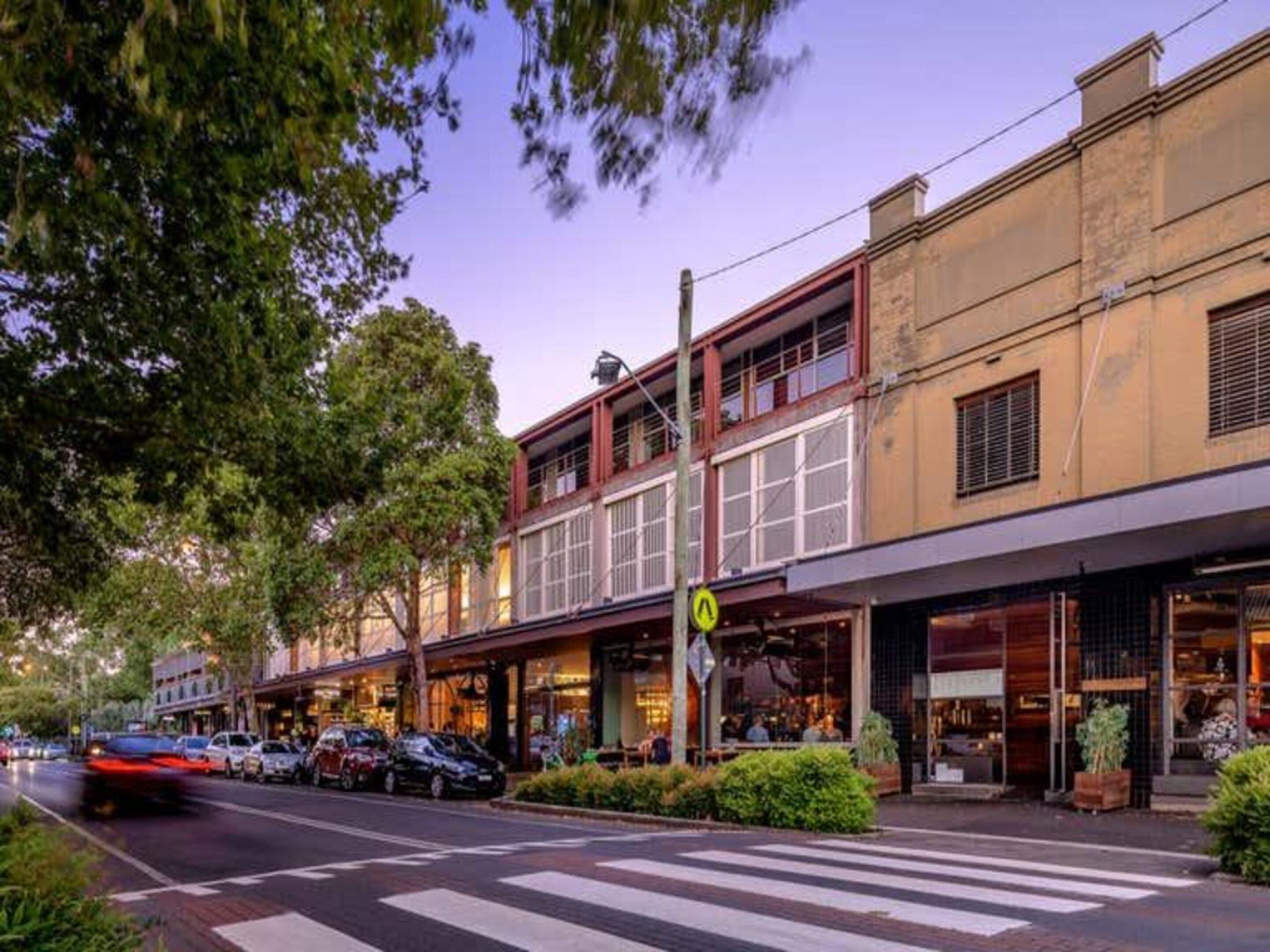 A street view with a row of buildings, some with storefronts, and cars parked along the side.