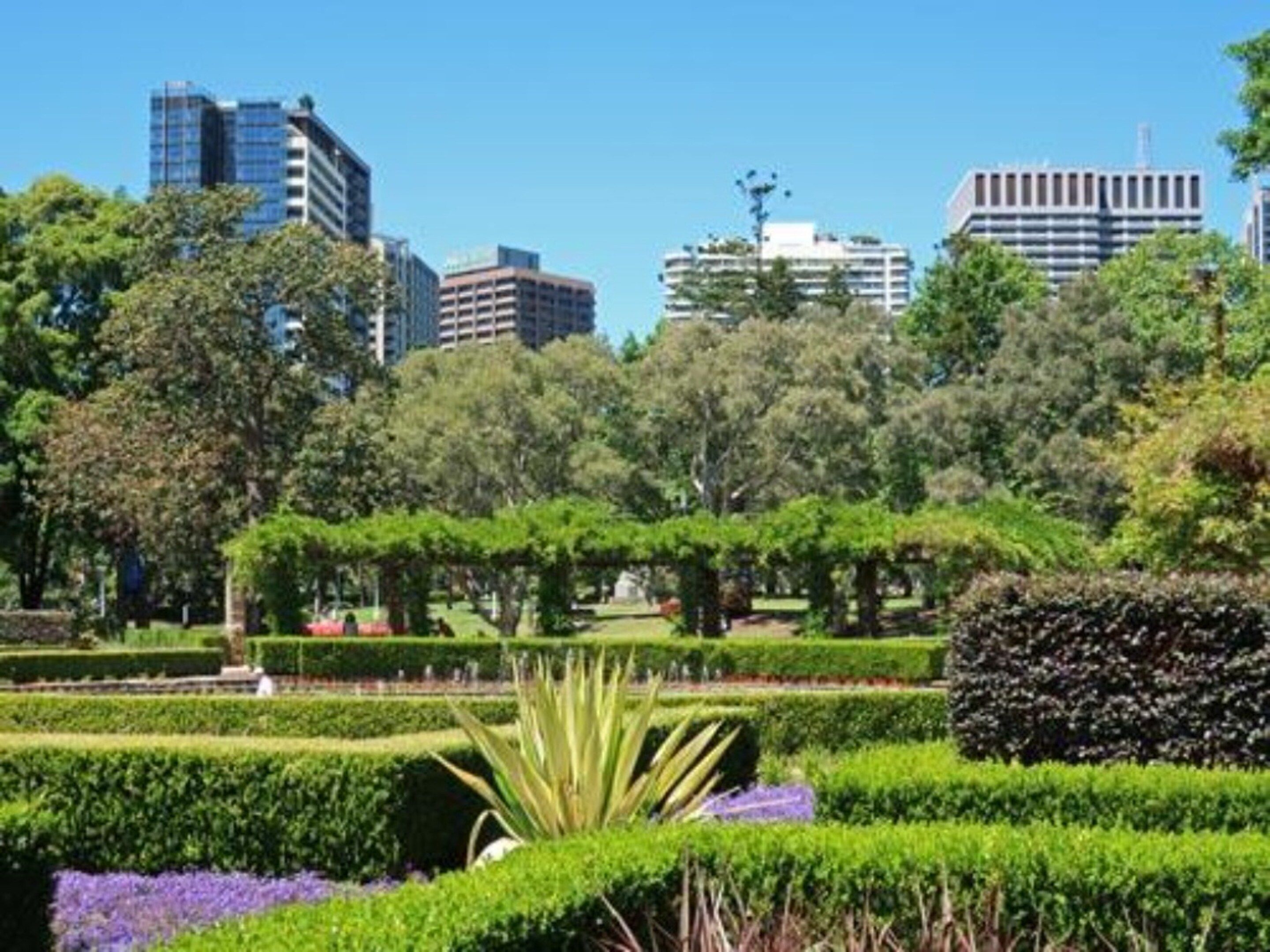 A park with manicured hedges and trees, surrounded by urban buildings.