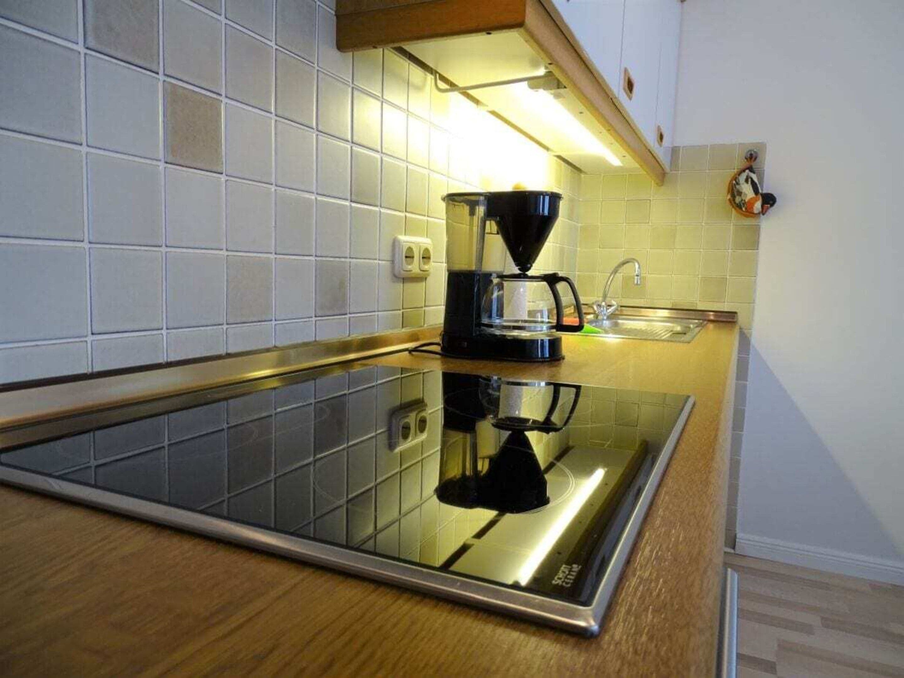A modern kitchen with a black induction cooktop, a coffee maker, and a stainless steel sink.