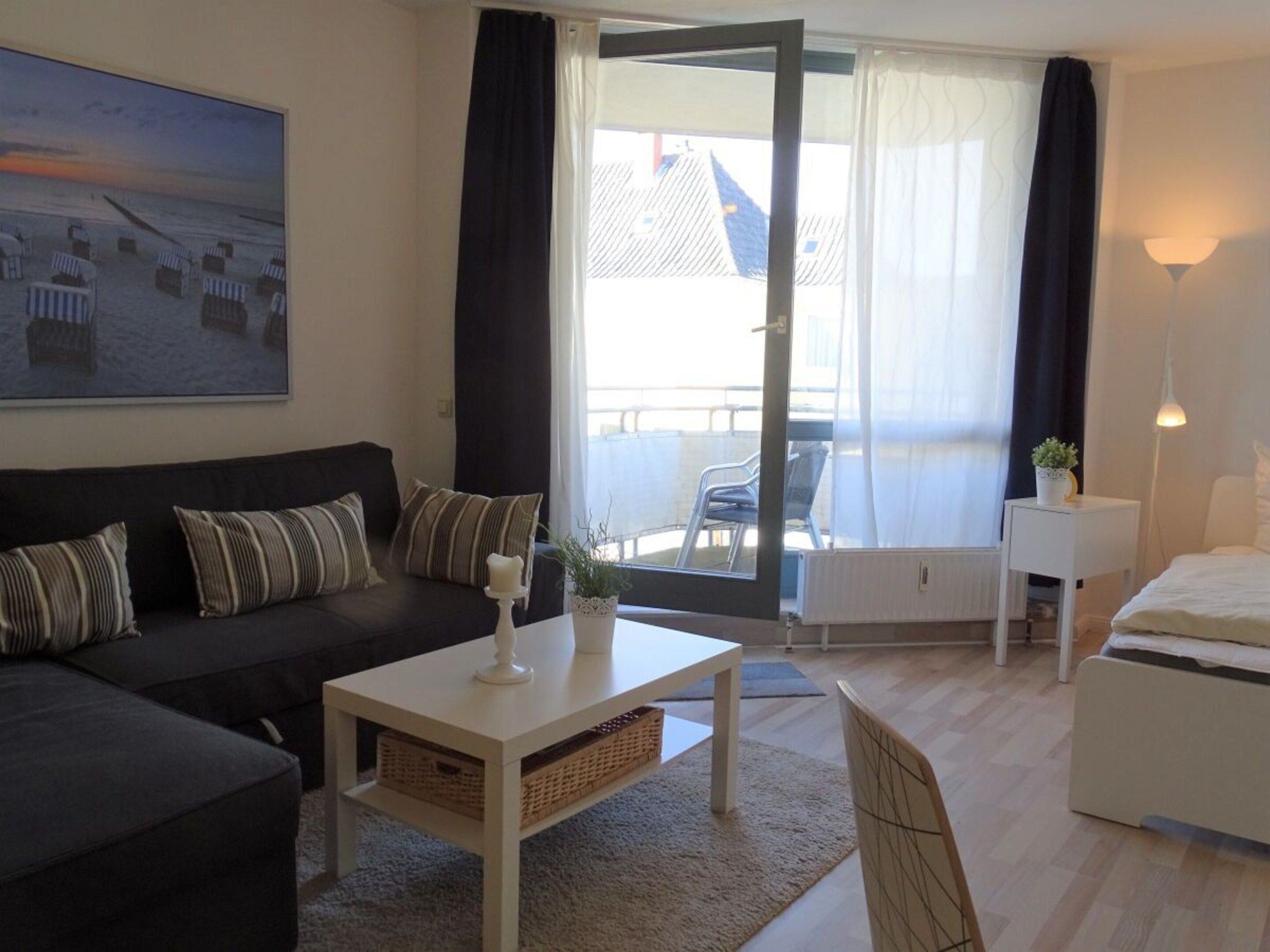 A modern living room with a sofa, a coffee table, a side table with a lamp, and a bed.