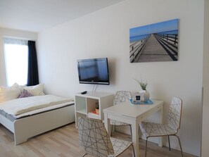 A hotel room with a bed, a TV, a desk with chairs, and a painting of a pier. - Beach House Villa 9 (Dahme)