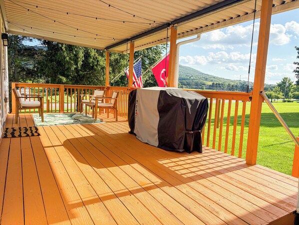 A covered outdoor deck with wooden flooring, a table with a tablecloth, and a flag.