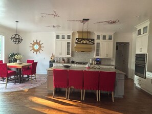 A spacious kitchen with white cabinets, a central island with red chairs, and a dining area with a red table and chairs.