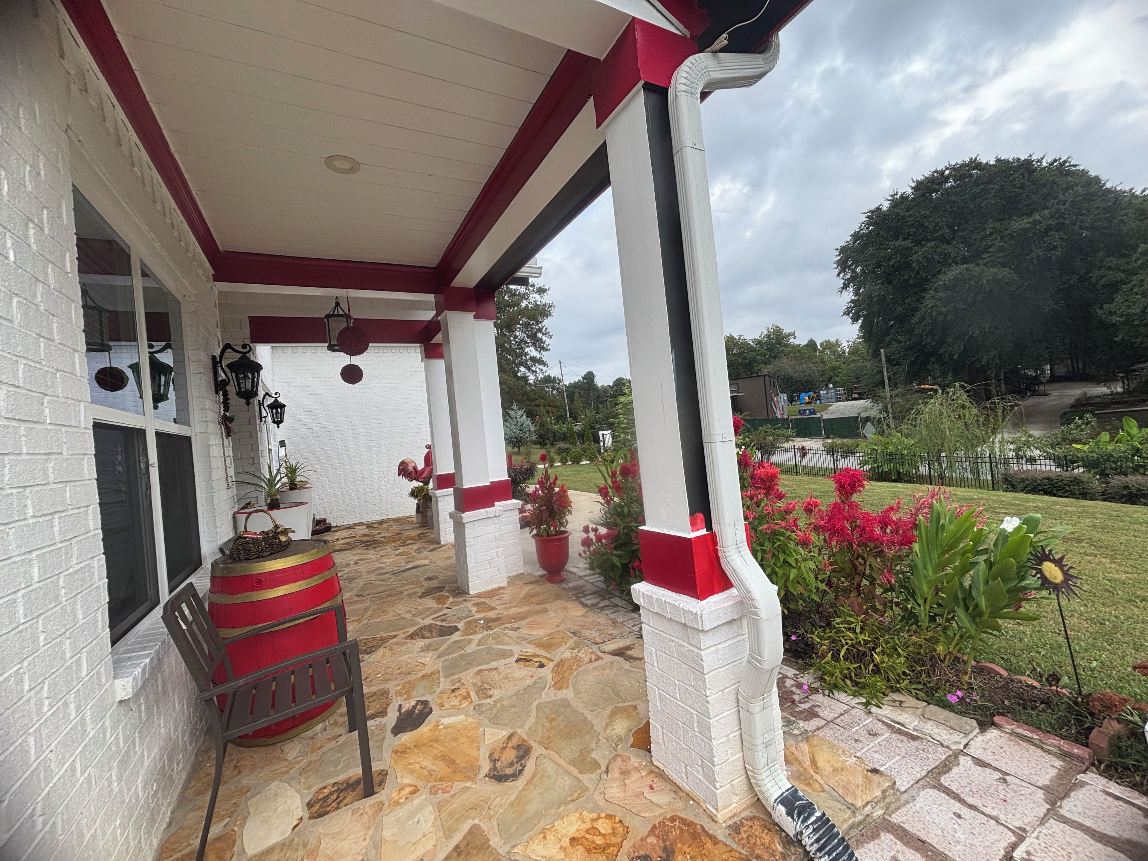 A covered porch with stone flooring, a red and white column, and potted plants.