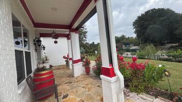 A covered porch with stone flooring, a red and white column, and potted plants.