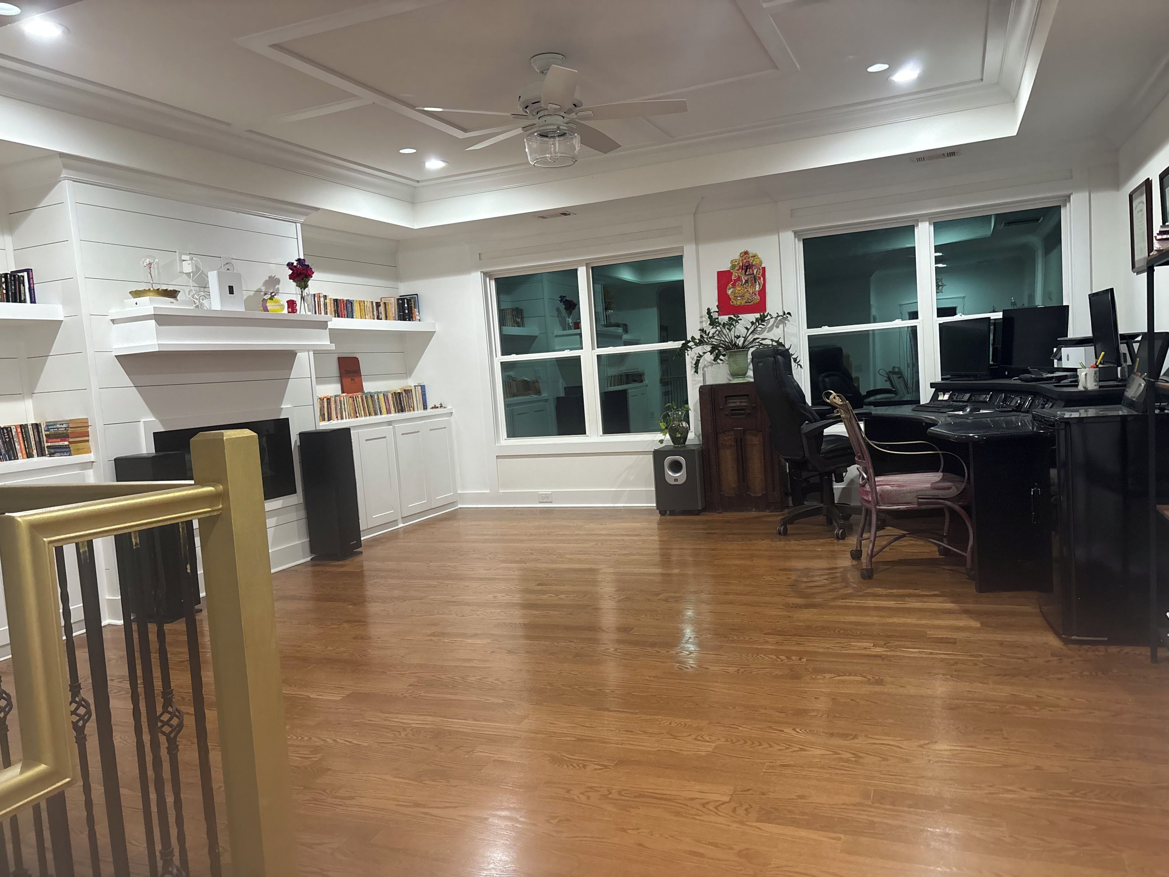 A spacious room with a wooden floor, a desk with a computer, a chair, and a bookshelf filled with books.