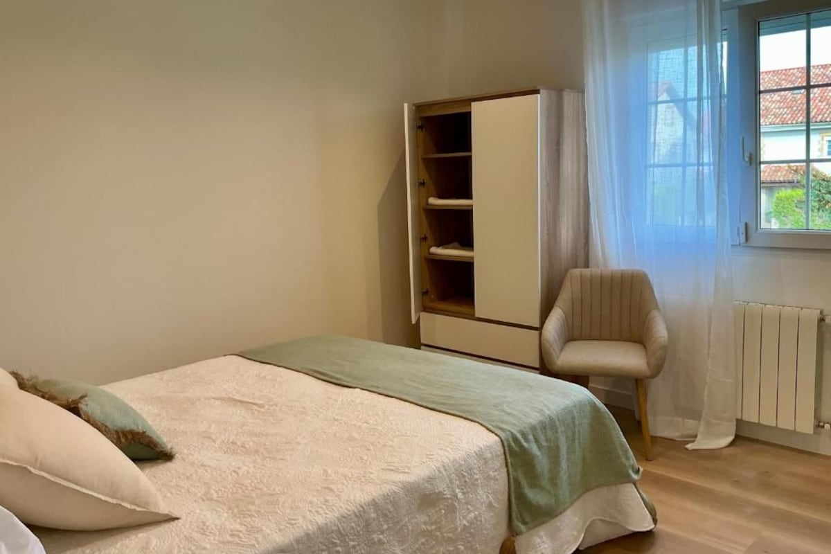 Ein Schlafzimmer mit einem Bett, einem Kleiderschrank, einem Sessel und einem Fenster.