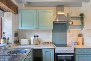 A kitchen with light blue cabinets, a stainless steel range hood, a built-in oven, and a dishwasher. - 1-bedroom Cornish Hideaway (Bodmin)