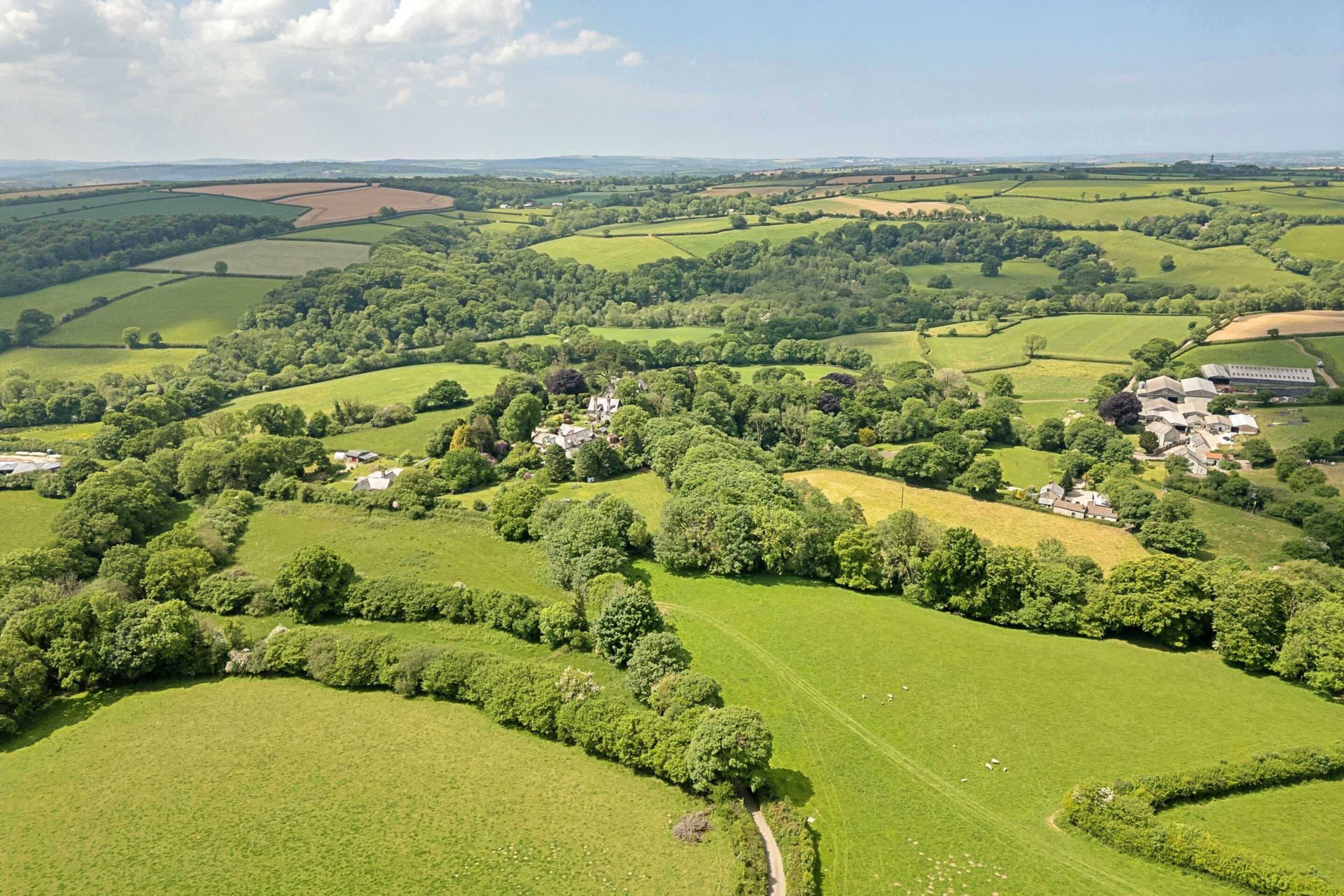 A rural landscape with rolling green fields, scattered houses, and a clear sky.