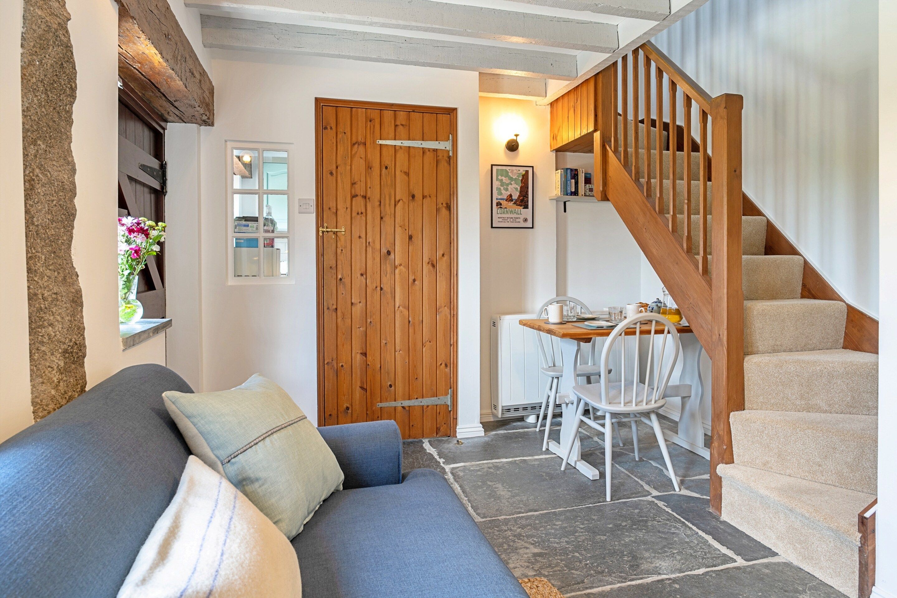 Una sala de estar acogedora con un sofá, una mesa de comedor con sillas, una escalera de madera y una puerta.