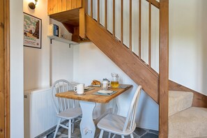 A dining area with a wooden table, white chairs, and a staircase. - 1-bedroom Cornish Hideaway (Bodmin)