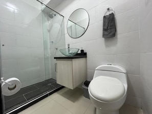 Un baño con cabina de ducha de vidrio, un inodoro, un lavabo con recipiente de vidrio y un espejo.