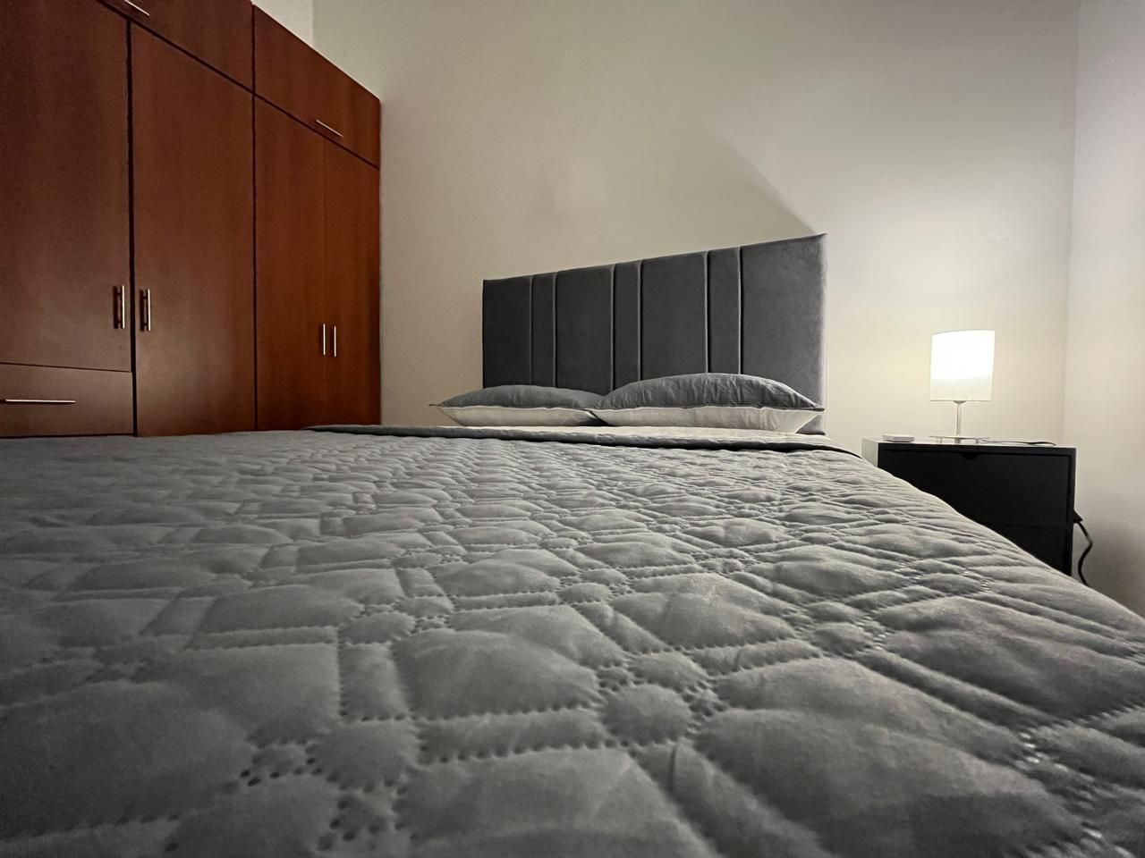 Un dormitorio con una cama grande, un armario y una mesita de noche con una lámpara.