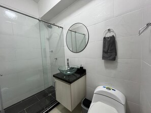 A modern bathroom with a glass shower enclosure, a glass sink, a toilet, and a mirror.