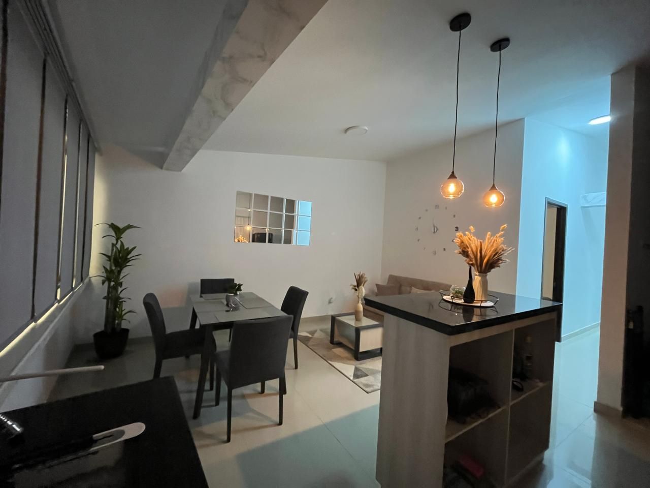 Una cocina moderna con comedor, una isla integrada, iluminación colgante y una planta en maceta.