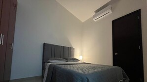 Quarto com cama, mesa de cabeceira, ar-condicionado fixado na parede e uma porta.