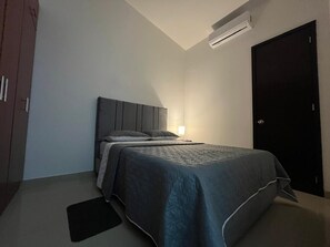 Un dormitorio con cama, mesita de noche, aire acondicionado de pared y una puerta.
