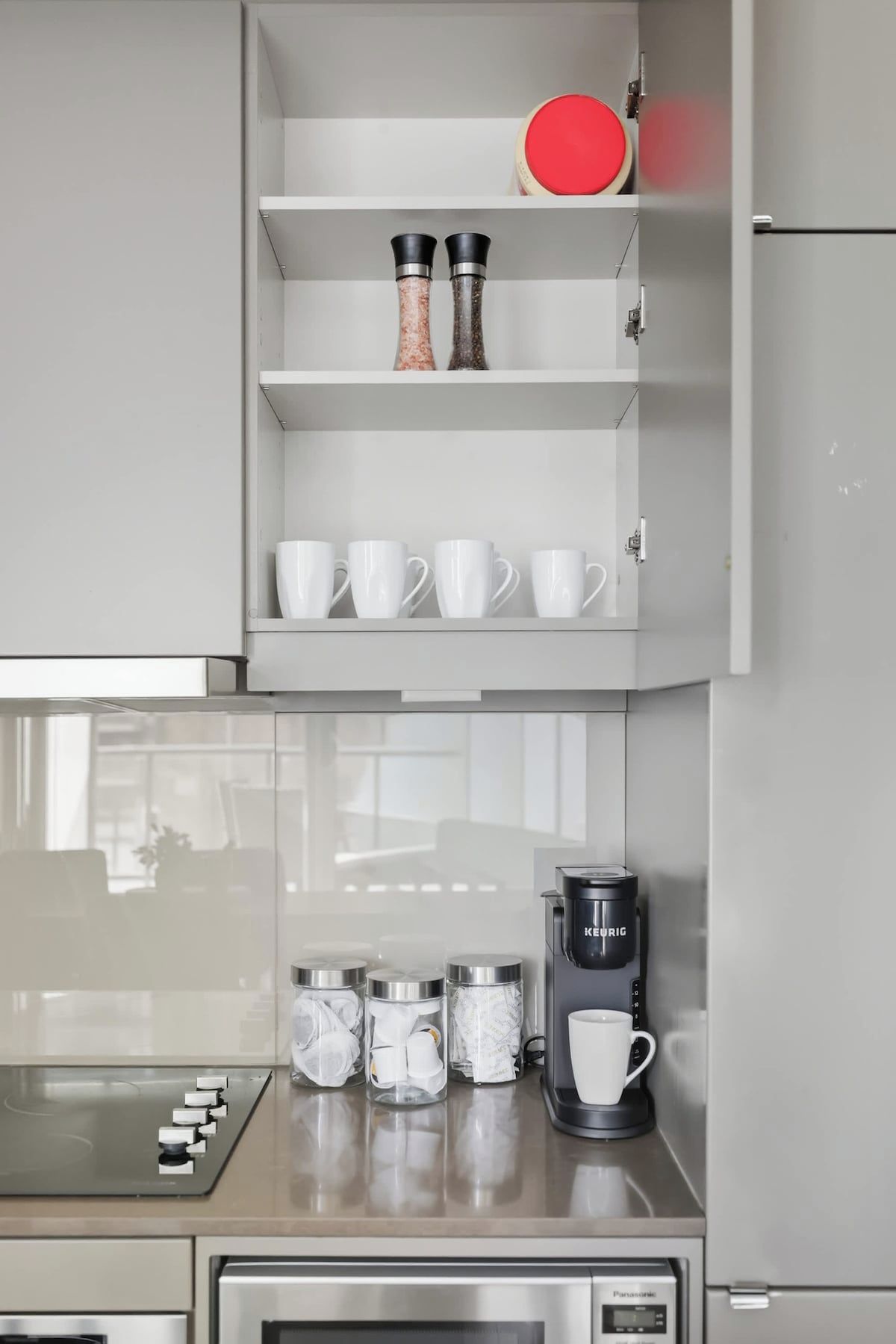 Una cocina equipada con cafetera integrada, microondas y un mueble con especieros y tazas blancas.