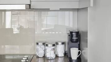 Una cocina equipada con cafetera integrada, microondas y un mueble con especieros y tazas blancas.