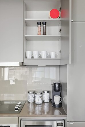 Una cocina equipada con cafetera integrada, microondas y un mueble con especieros y tazas blancas.