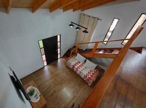 A spacious room with a wooden floor, a staircase, and a window with curtains. - Alojamiento Iguazú Yvyra  (Puerto Iguazú)