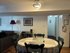 Un comedor con una mesa redonda, sillas, una lámpara y una cafetera.