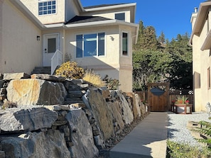 A two-story house with a stone retaining wall, a wooden gate, and a pathway leading to the entrance.
