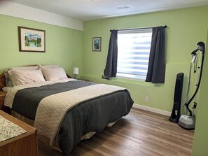 Un dormitorio con cama, una mesita de noche, una ventana con cortinas, un aspirador y dos cuadros en la pared.