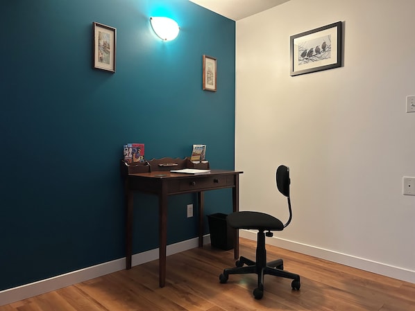 A room with teal walls, a wooden desk, a black office chair, and framed pictures on the walls.