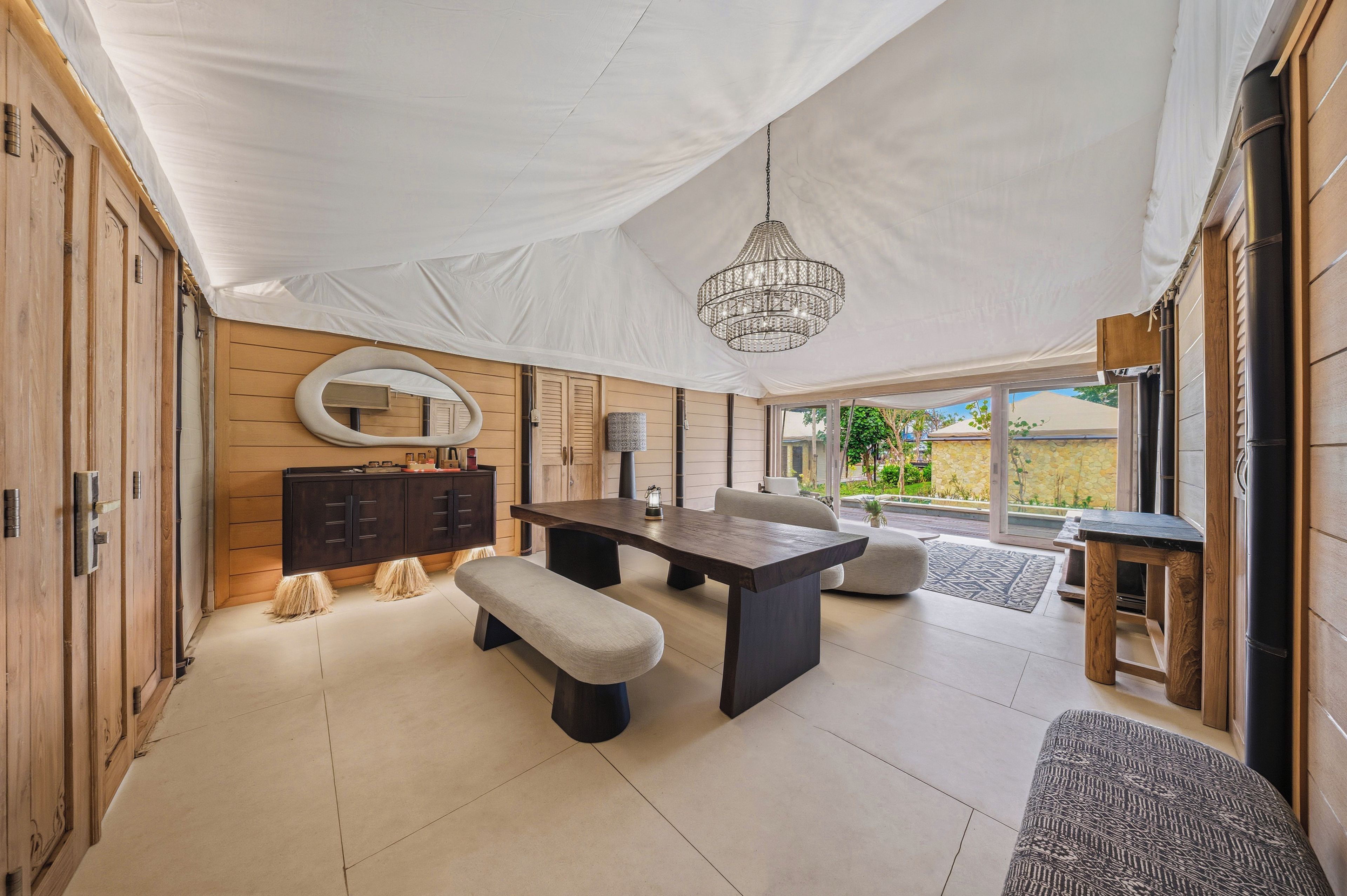 Una habitación amplia con una gran mesa de comedor, asientos tipo banco, un candelabro y vistas a través de un ventanal.