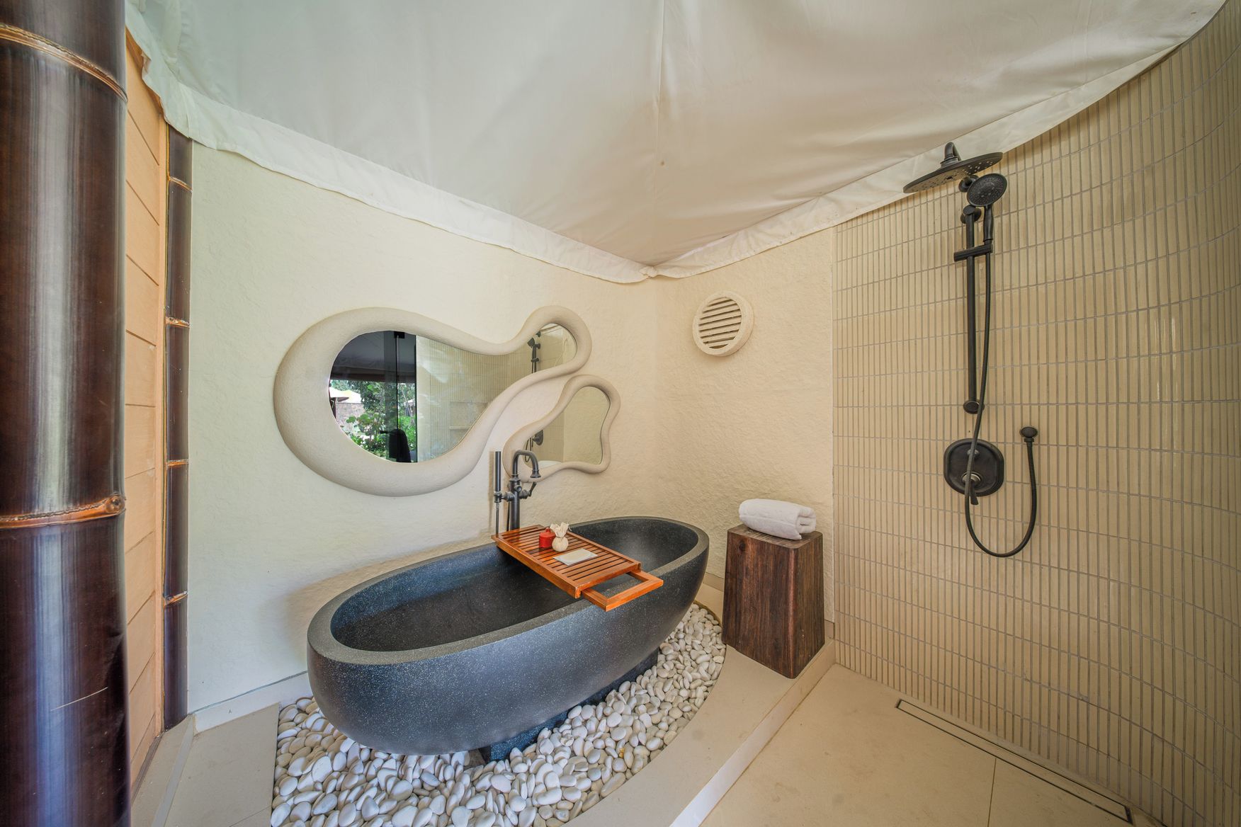 Une salle de bain avec un grand lavabo en pierre, un plateau en bois, un miroir, une serviette et un espace douche.