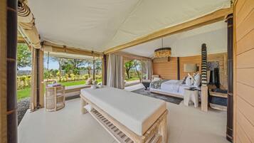 A spacious tented room with a large bed, a bedside table, and a view of the outdoors.