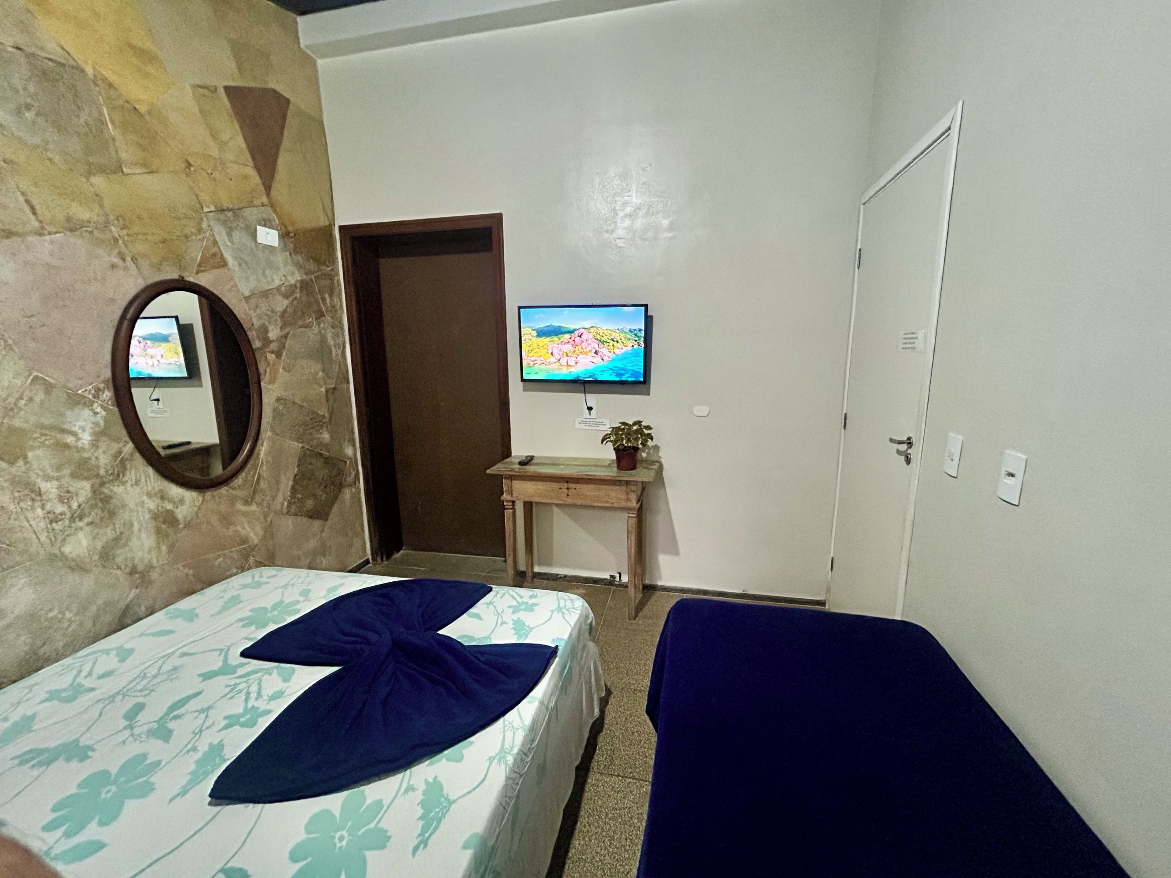 Een hotelkamer met een stenen muur, een bed met bloemenbedrukking, een televisie op een houten standaard en een deur.