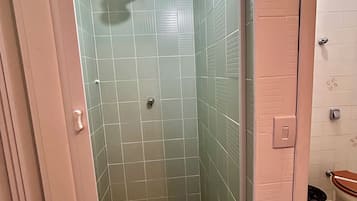 Um chuveiro pequeno e fechado, com azulejos verdes e uma luminária branca no teto.