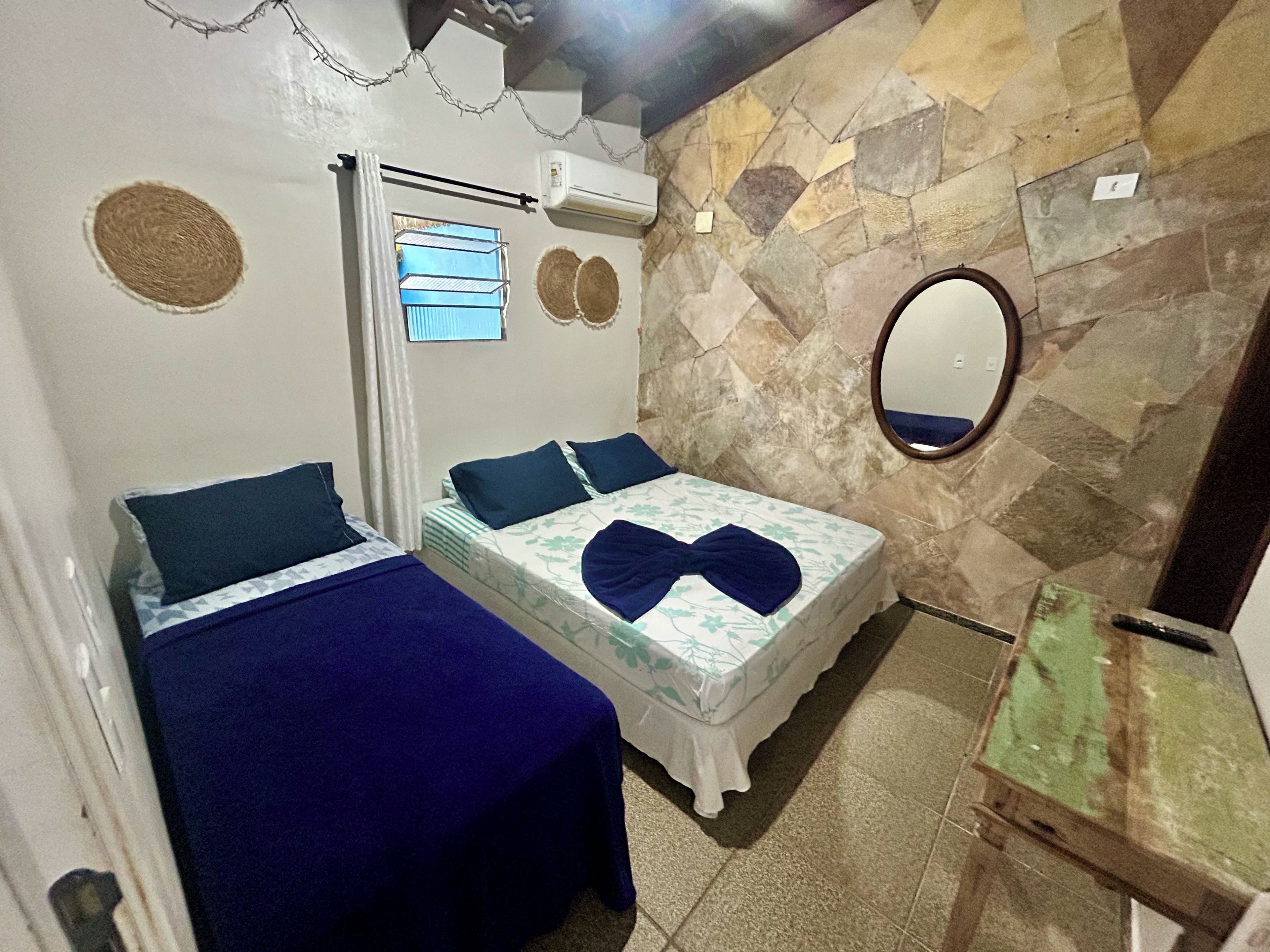 A bedroom with two beds, a stone wall, a mirror, and an air conditioning unit.
