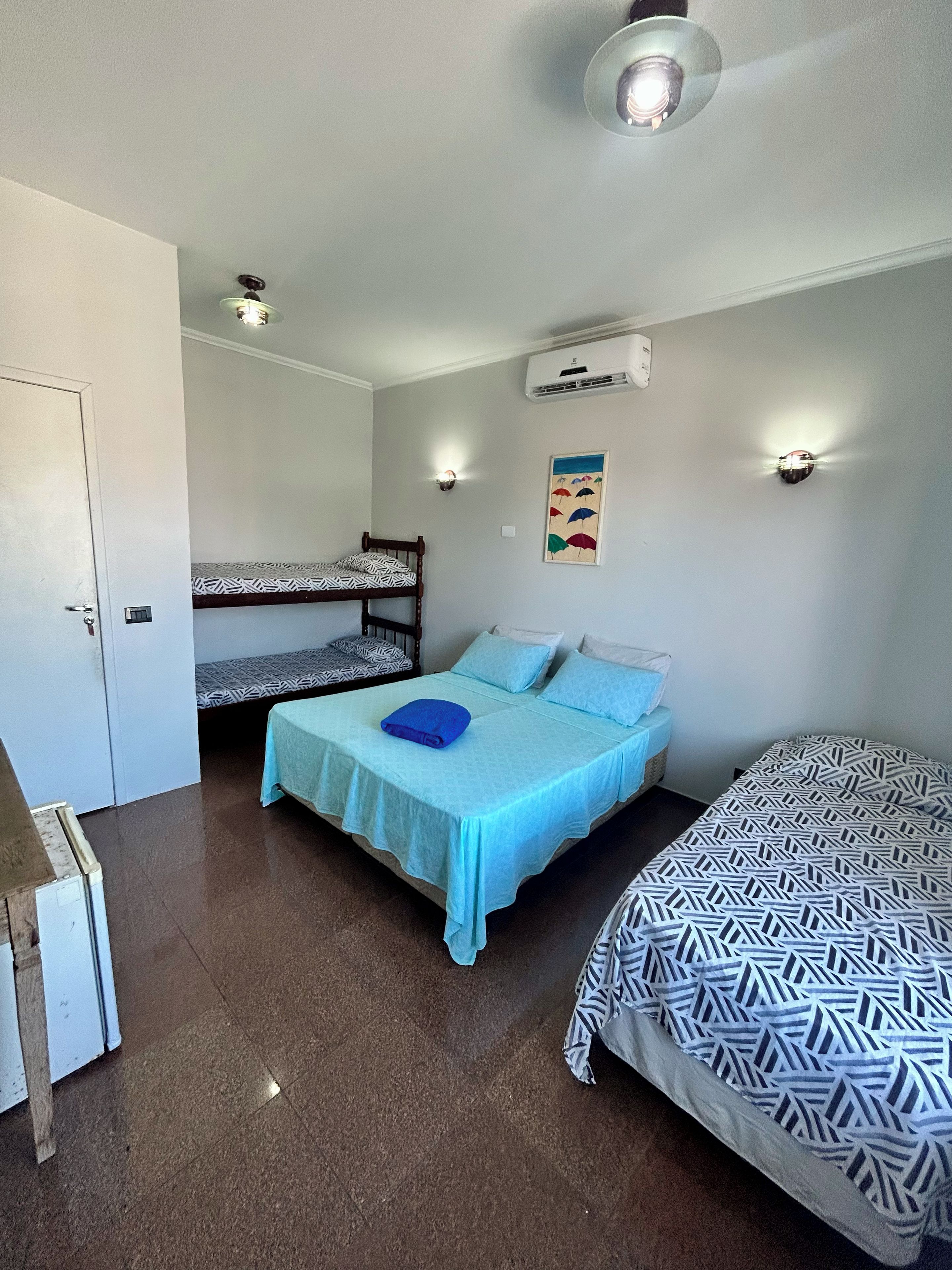 Habitación con literas, una cama individual y un escritorio. Cuenta con ventilador de techo, unidad de aire acondicionado y una lámpara fijada a la pared.